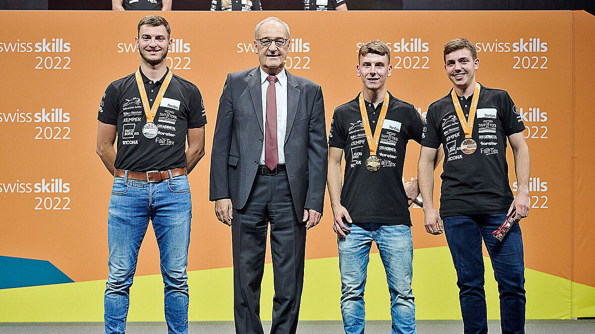 Remise des prix aux constructeurs métalliques avec les félicitations du Conseiller fédéral Guy Parmelin : les trois heureux lauréats sur le podium. De gauche à droite: Mirco Hegner (2e), Julian Gemperli (1er), Samuel Sturzenegger (3e).