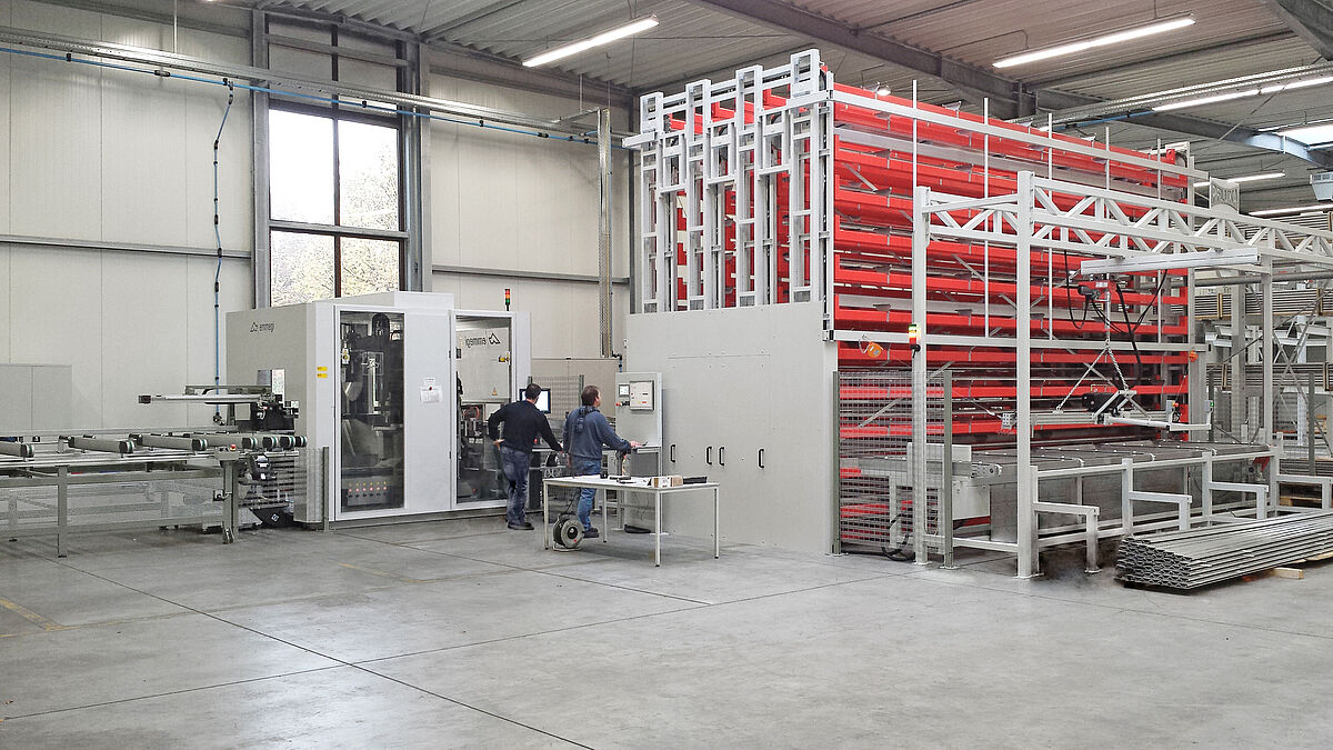 Un magasin de barres Paternoster de Karl Pflumm GmbH charge automatiquement le centre d’usinage de profilés Emmegi Quadra à l’arrière-plan.