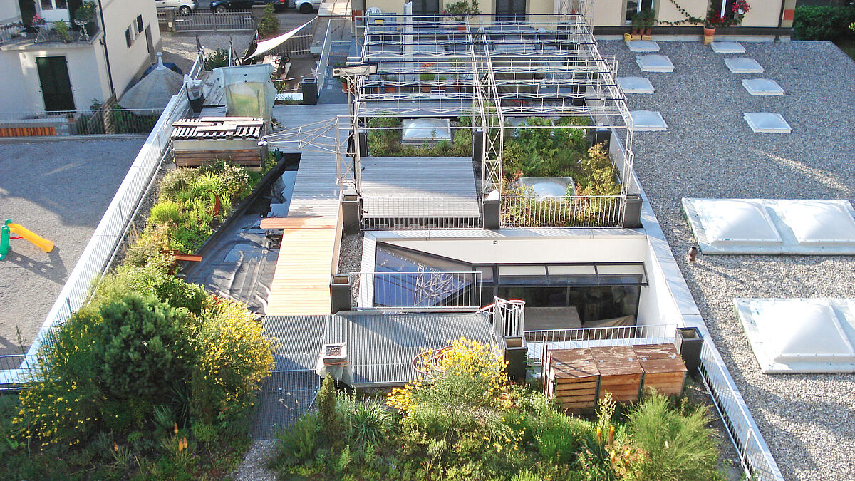 Les toits plats rénovés : végétalisation généreuse à côté de terrasses en bois et d’un étang. Garde-corps à lattes fixé aux bacs à plantes. Certains supportent les montants des attelles des pergolas non encore plantées. 