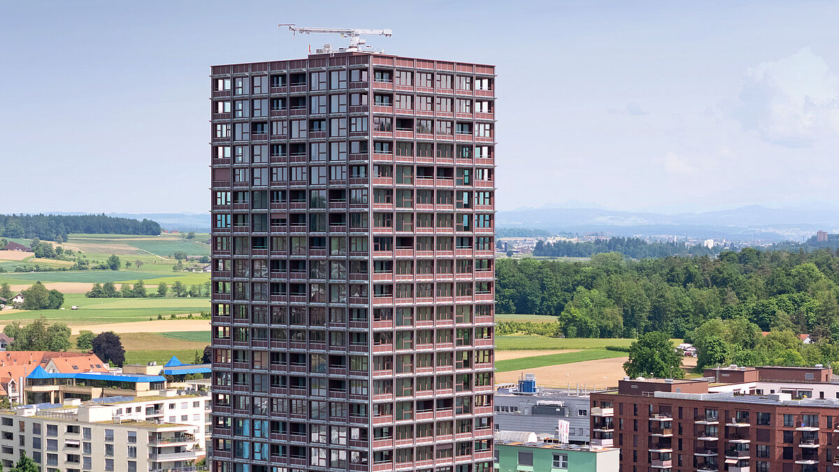 L’immeuble H1 de 24 étages à Regensdorf-Watt (Zurich) : une construction hybride bois moderne. Des fenêtres en bois et des panneaux métalliques forment l’enveloppe du bâtiment, alors que des modules solaires en porte-à-faux produisent de l’électricité et offrent une protection contre les intempéries.