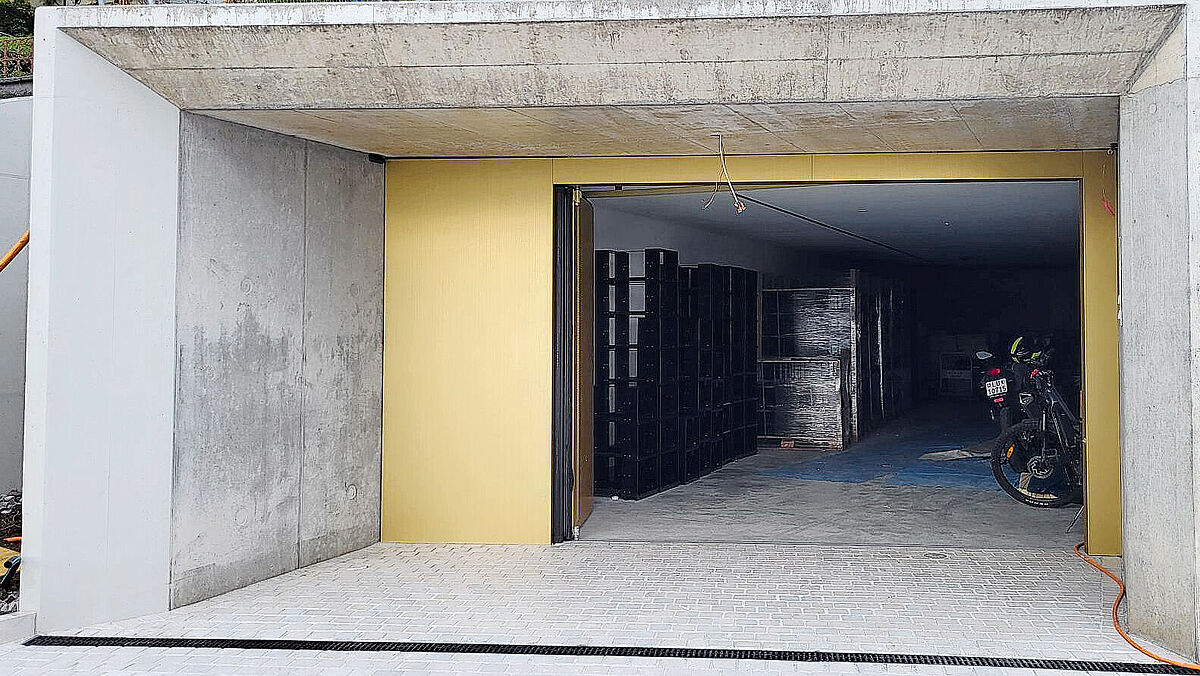 Entrée du garage avec portail pliant automatisé. Le revêtement extérieur en tôle a été posé dans l’usine du constructeur du portail.