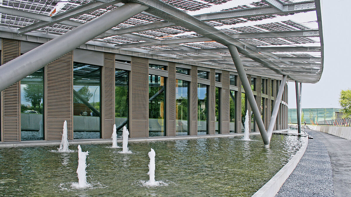 Der Rhythmus aus Fenster- und Lüftungselementen bestimmt das Erscheinungsbild der Fassade. Das Vordach mit integrierter Photovoltaik und das Wasserbecken schaffen ein kühles Mikroklima vor der Fassade und reduzieren dadurch den Kühlungsaufwand.