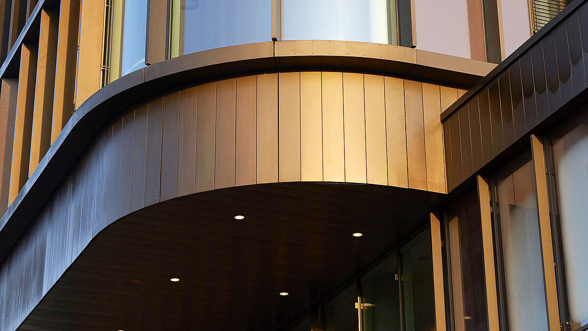 Des tôles fines laminées et cintrées en cuivre patiné ainsi que des profilés en aluminium anodisé dans la même teinte caractérisent ce revêtement de façade aux reflets dorés ou bruns chauds. 