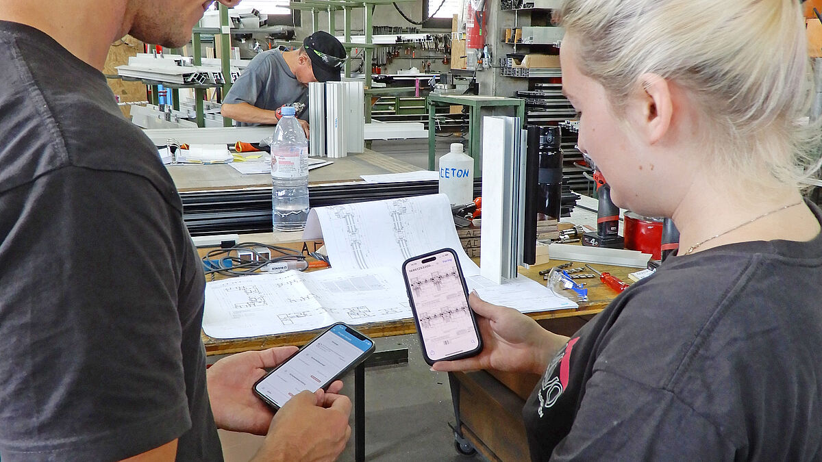 Alles auch auf dem Handy: Zwei Mitarbeitende in der Werkstatt erklären die AM Suisse App. 
