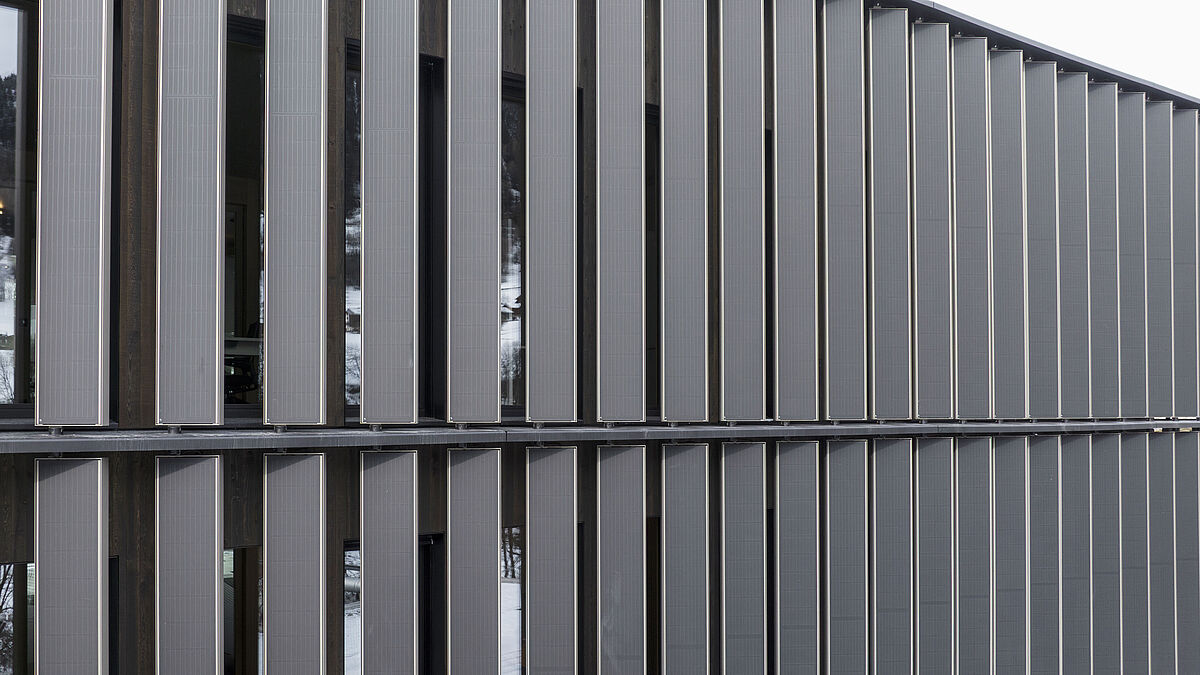 Derrière les lamelles se trouve la façade chaude composée de fenêtres en bois et verre à isolation thermique.