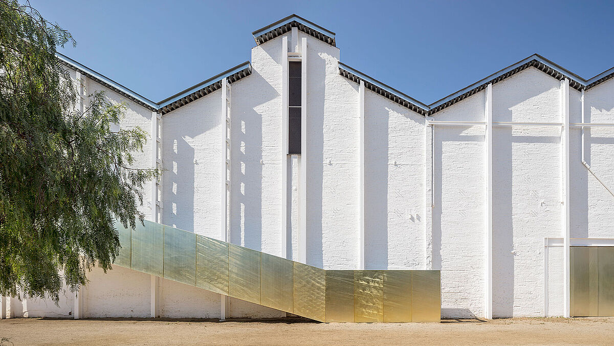 Un escalier métallique, en forme de poutre ascendante, dessert le bâtiment culturel à l’arrière.