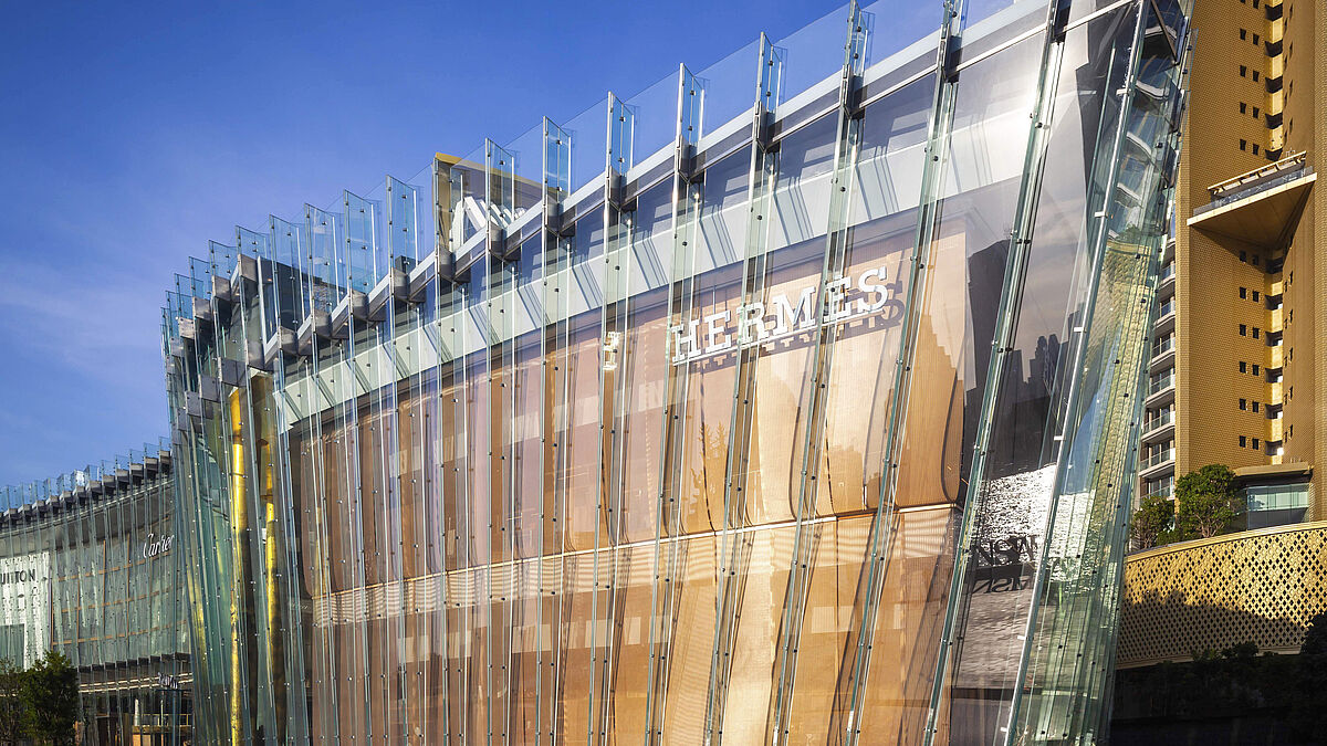 Die frei hängende Innenfassade aus Metallgewebe verbindet die beiden Store-Ebenen optisch miteinander und folgt wie ein Vorhang der dynamischen Linienführung der Fassade.