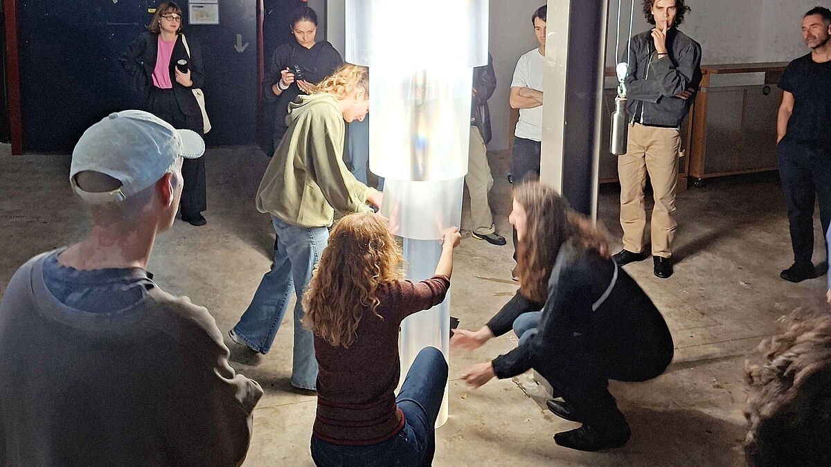 Letzte Vorbereitungen für die finale Vorführung. Das zylindrisch geschichtete Objekt aus Prismafolien und der innenseitig absenkbare Leuchtkörper am Aufzug werden in Position gebracht. Letzte Vorbereitungen für die finale Vorführung. Das zylindrisch geschichtete Objekt aus Prismafolien und der innenseitig absenkbare Leuchtkörper am Aufzug werden in Position gebracht.